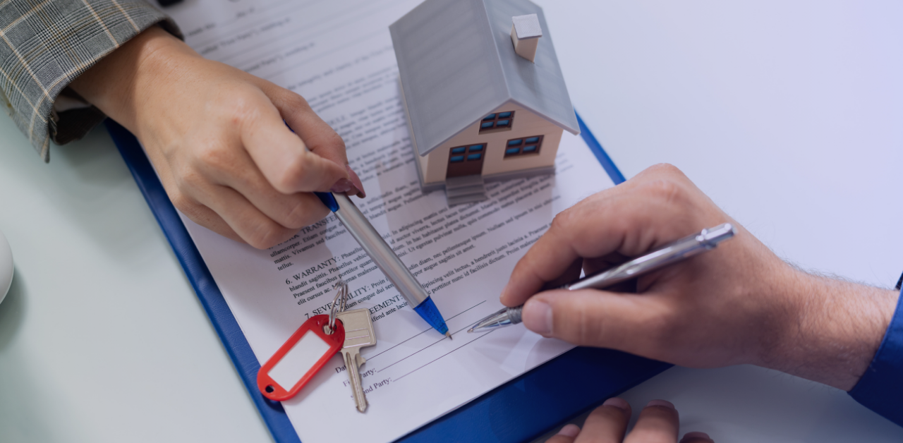 Hands point to a property contract with a model home and keys on the table