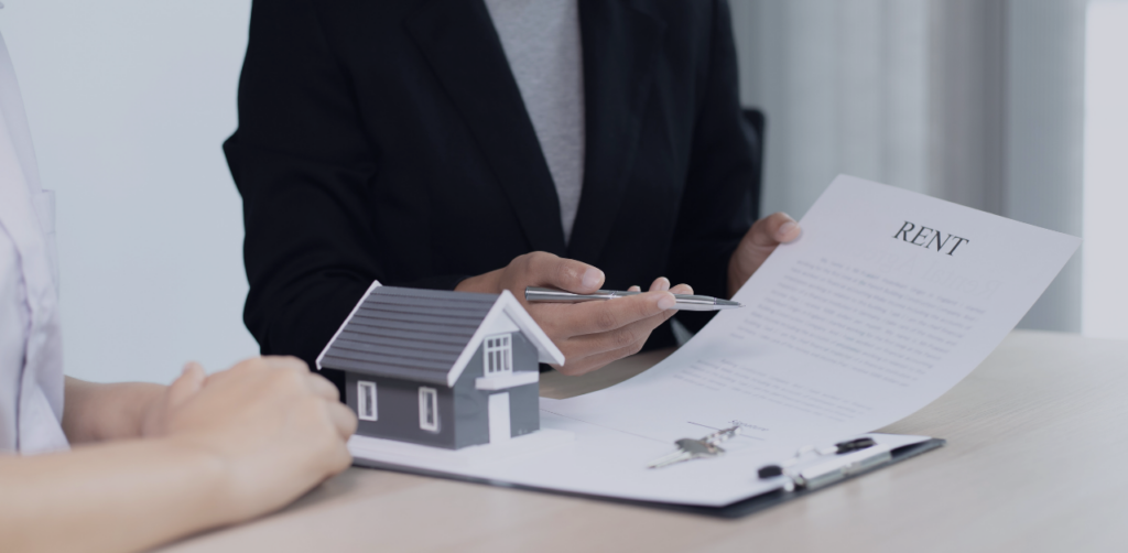 Agent reviews a rental agreement with a client beside a model house and keys