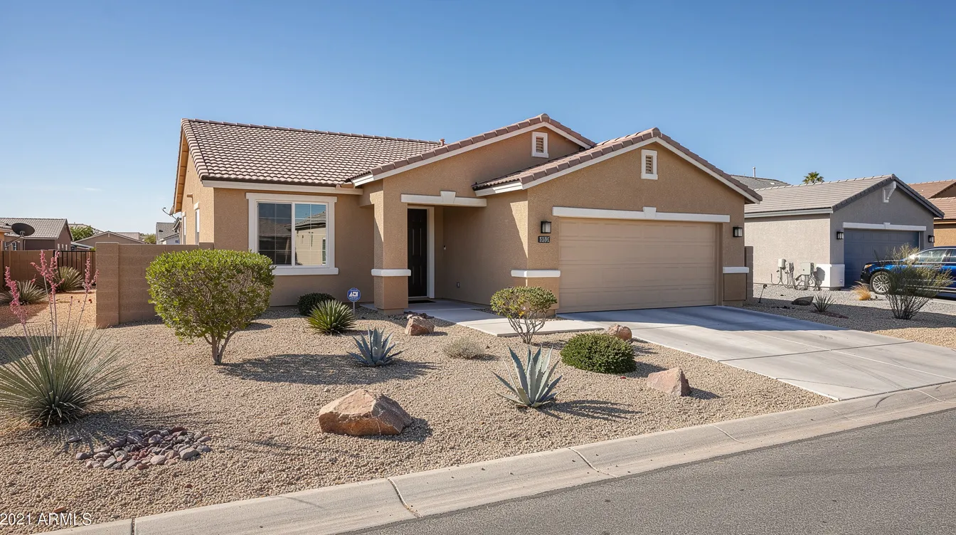 Beige suburban house with a tiled roof, attached garage, gravel yard, shrubs, agave plants, and decorative rocks